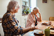 © Marko Geber - Senior Caucasian woman is having neck pain while eating breakfast with her husband in the morning in the kitchen
