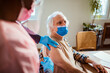 © Marko Geber - Senior Caucasian man getting vaccinated by his caregiver in the living room at home