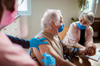 © Marko Geber - Senior Caucasian man comforted by his wife while getting vaccinated by his caregiver in the living room at home
