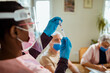 © Marko Geber - Young African American caregiver preparing a vaccine for her patient in their home