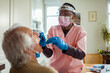 © Marko Geber - Young African American caregiver testing a senior patient for the coronavirus at home