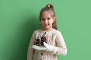 Canvas Print - Cute little girl in knitted sweater with fir cones on green background