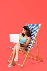 Sticker - Beautiful Asian woman using laptop in deck chair on red background