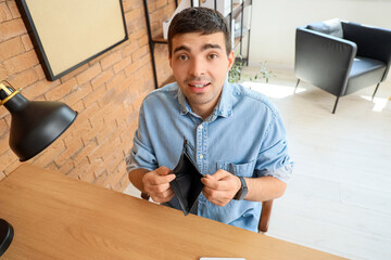 Wall Mural - Upset young man with empty wallet in office