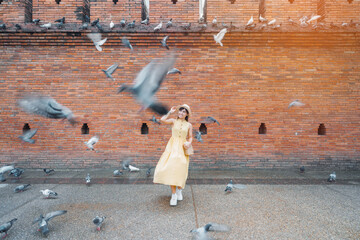 Young asian woman traveler in Yellow dress with hat and bag traveling on Tha Pae Gate, Tourist visit at the old city in Chang Mai, Thailand. Asia Travel, Vacation and summer holiday concept