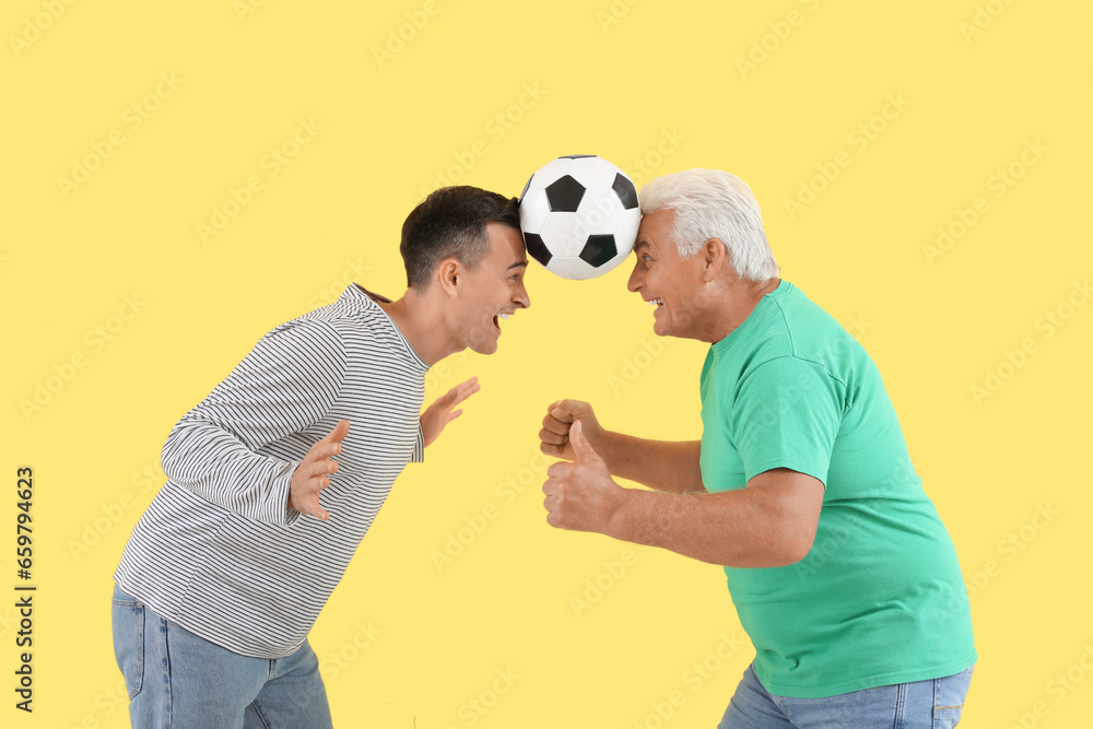 Young man and his father playing with soccer ball on yellow background