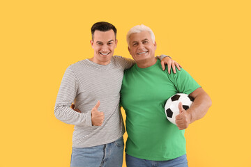 Poster - Young man with his father and soccer ball hugging on yellow background