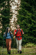 © La Famiglia - A couple with backpacks and walking sticks hiking in nature.