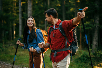 Wall Mural - A multicultural pair with backpacks and walking sticks discover the beauty of the outdoors, their beaming smiles mirroring their excitement for the journey ahead