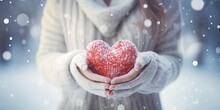 Winter Snow Christmas Valentine Background Greeting Card - Closeup Of Woman With Gloves Holding A Rod Heart In Her Hands, Defocused Blurred Bacground With Snowflakes