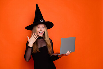 Sticker - Photo portrait of lovely blonde teen lady hold laptop amazed hand dressed black halloween garment isolated on orange color background