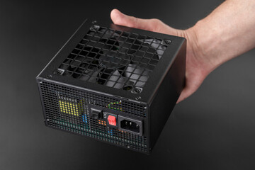 Power supply of computer and its components with cooling system. AC power supply unit of heavy-duty processor for gaming or professional computer in hands of a master assembler on black background