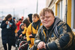 One young caucasian teen with down syndrome is smiling on the street against the background of other people. World genetic diseases day and syndrome down concept.