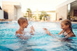 © Minet - In a sunlit modern villa, a young brother and sister joyfully splash and play in the pool, basking in the warmth of a perfect summer day
