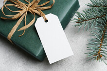 Blank Gift Tag Card Mockup With Christmas Gift Box On Grey Background, White Label With Copy Space For Design Presentation