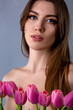 Close-up studio portrait of a beautiful sexy slim young caucasian brown-haired girl topless holding bouquet of pink tulips