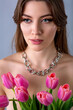 Close-up studio portrait of a beautiful sexy slim young caucasian brown-haired girl topless with silver chain necklace holding bouquet of pink tulips