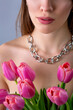 Close-up studio portrait of a beautiful sexy slim young caucasian brown-haired girl topless with silver chain necklace holding bouquet of pink tulips