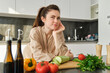 Portrait of pretty woman in bathrobe, standing in kitchen with thoughtful face, posing near vegetables and bottle of oil, thinking what food to prepare, making salad, eating healthy