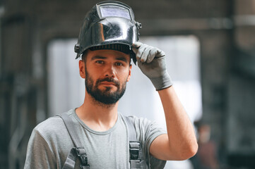 Welder man in safety helmet. Young factory worker in grey uniform