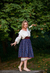 beautiful blonde ukrainian woman in national traditional cloth embroidery posing on wooden bench in forest