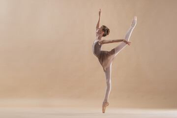 Wall Mural - Beautiful young girl professional student ballerina in pointe shoes and a leotard on a light beige background.