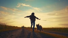 Teen Girl Running With A Dog In The Park. Happy Family Freedom A Kid Dream Concept. Silhouette Of A Teenage Girl Running Along The Road In The Park At Sunset View From The Back Sun With A Shaggy Dog
