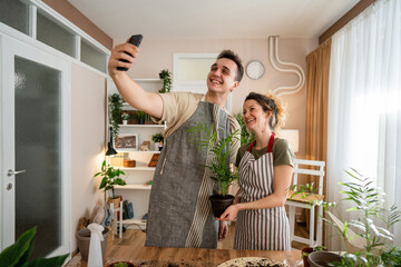 Wall Mural - Couple caucasian man and woman wife and husband planting flowers together taking care of home plants real people domestic life family gardening concept take selfie photo with smartphone copy space