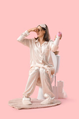 Poster - Displeased young woman in pajamas with air freshener sitting on toilet bowl against pink background