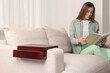 © New Africa - Wooden armrest table on sofa in room. Woman reading book at home, selective focus