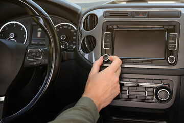 Wall Mural - Listening to radio while driving. Man turning volume button on vehicle audio in car, closeup