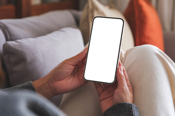 Poster - Mockup image of a woman holding mobile phone with blank desktop white screen whilesitting on a sofa at home