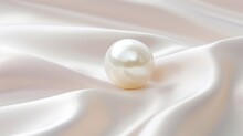 Single Pearl On A White Satin Background. The Pearl Is Round And Shiny, Reflecting The Light. The Satin Fabric Has Soft Curves And Folds, Creating A Contrast With The Pearl.