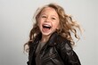 Portrait of a laughing little girl in a leather jacket on a gray background