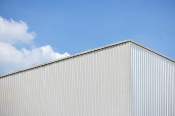 Poster - metal sheet factory warehouse against blue sky background. silver corrugated steel industrial roof.