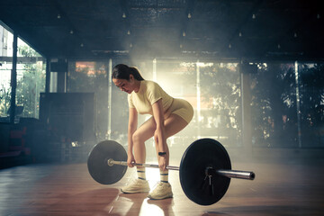 Young woman doing deadlift with heavy bar in gym, strong female athlete with muscular body lifting weights, exercising with barbell.