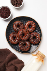 Wall Mural - Chocolate donuts on plate, bottle with milk and bowls on white background, top view