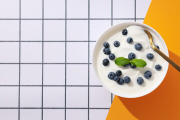 Wall Mural - Bowl with yogurt and berries on white and yellow background, space for text