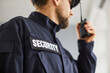 © Studio Romantic - Close up cropped portrait of confident male security guard standing indoors. Bearded guardian man in blue uniform talking by the walkie talkie and looking to the side. Selective focus.
