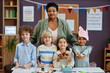 © Seventyfour - Portrait of senior Black woman as female teacher posing with diverse group of children in preschool all looking at camera