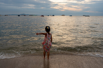 Small girl on the sea shore against sunset sky.