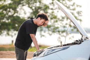 Wall Mural - A stressed Asia young man has a problem with his car breaking down. He looked annoyed because the engine has failed.