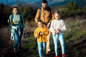 Wall Mural - Smiling family of four enjoying hiking in the meadow on the mountain.