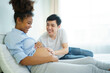 © DG PhotoStock - Happy cheerful husband and pregnant wife staying - relaxing together in bedroom, husband embracing or playing on pregnant wife tummy. Diverse ethnicity husband and wife lifestyles concept.