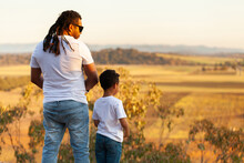 Aboriginal Father And Son Standing On Edge Of Cliff Looking Out Over Country Landscape