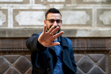 Young man hiding his smile with his hand in front of a wall