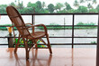 An empty cane chair overlooking the backwater in Allepey, Kerala during a rainy day in the monsoon season from a balcony near the waterfront in a luxury resort
