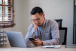 © PaeGAG - Freelance business man calling on mobile smartphone while working with laptop seriously stress depression, businessman mobile phone calling with customers. Smart phone conversation conference.