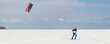 Panoramic view of many people friends enjoy riding kite surf board in warm suit on bright sunny winter day at frozen lake field snowy surface. Wintersport adrenaline fun adventure hobby acitivity