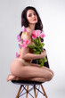 Studio portrait of a naked beautiful sexy slim young caucasian brunette girl covered with pink butterflies holding a bouquet of pink tulips sitting on chair attractively posing looking in camera